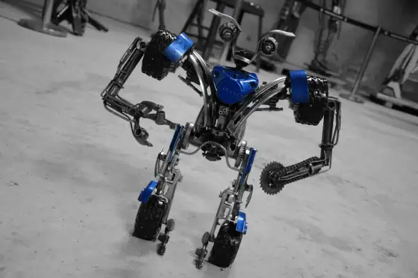 Robot z muzeum robotów Moszna, wykonany z metalowych części i ozdobiony niebieskimi akcentami, stoi na betonowej posadzce.