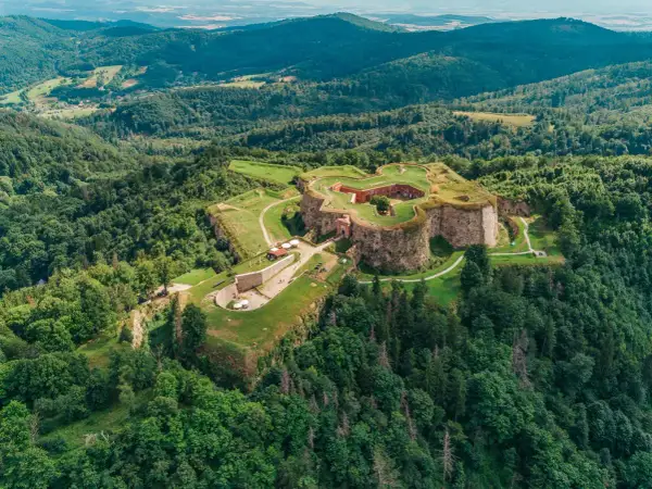 Forteca na wzgórzu, otoczona lasem, niczym srebrna góra w zieleni.