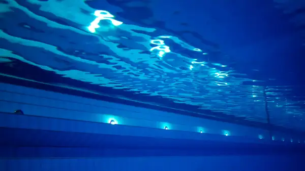 Podwodne ujęcie basenu sportowego na Termach Maltańskich. Błękitna woda, falująca powierzchnia i światła podwodne tworzą spokojną atmosferę.