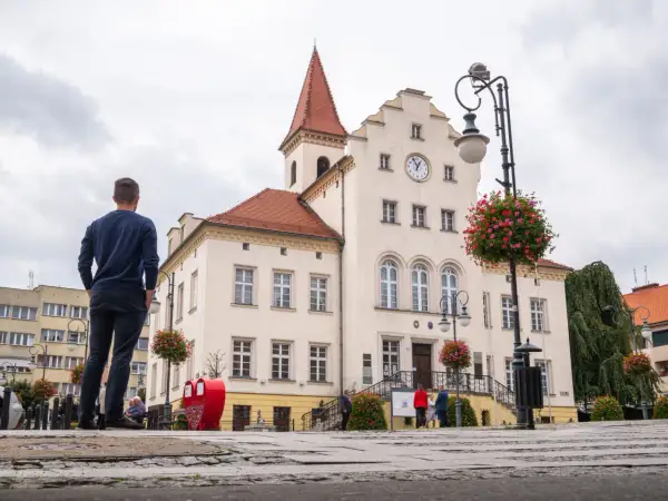 Mężczyzna patrzy na ratusz w Trzebnicy, jedno z głównych atrakcji miasta. W tle widać zegar i czerwone serca.