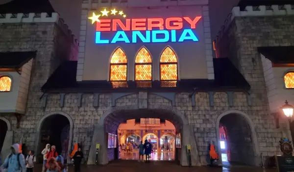 Wejście do Energylandii nocą, mimo deszczu, widać ludzi wchodzących pod łukiem.