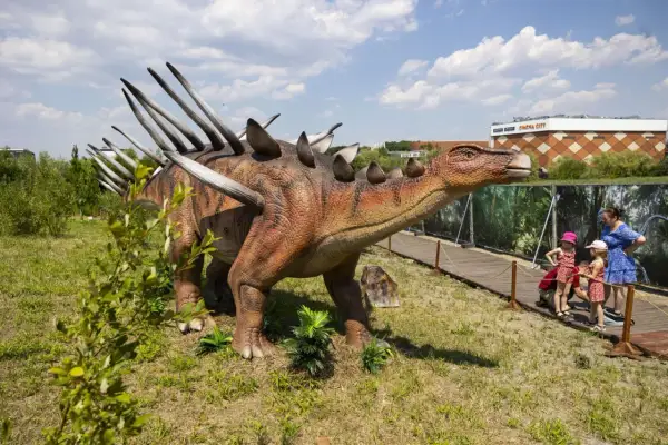 Model dinozaura w parku dinozaurów Kraków. Dzieci oglądają stegozaura.