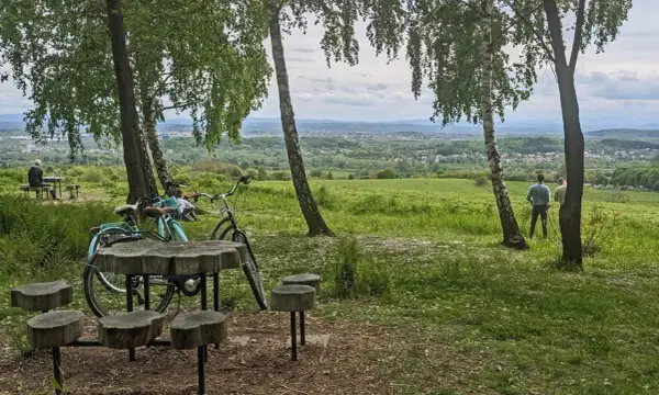 Idealny punkt widokowy Kraków. Dwa rowery, drewniany stolik i ławki czekają na turystów. W oddali rozciąga się malowniczy krajobraz.