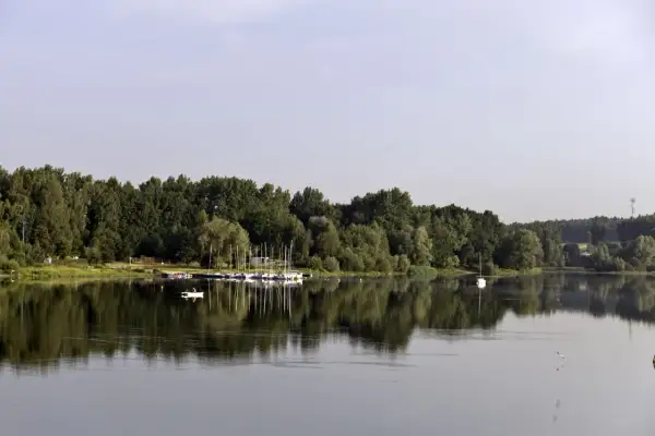 Spokojne jezioro Przeczyckie z odbijającymi się w wodzie drzewami i żaglówkami. Na wodzie widać samotną łódkę.